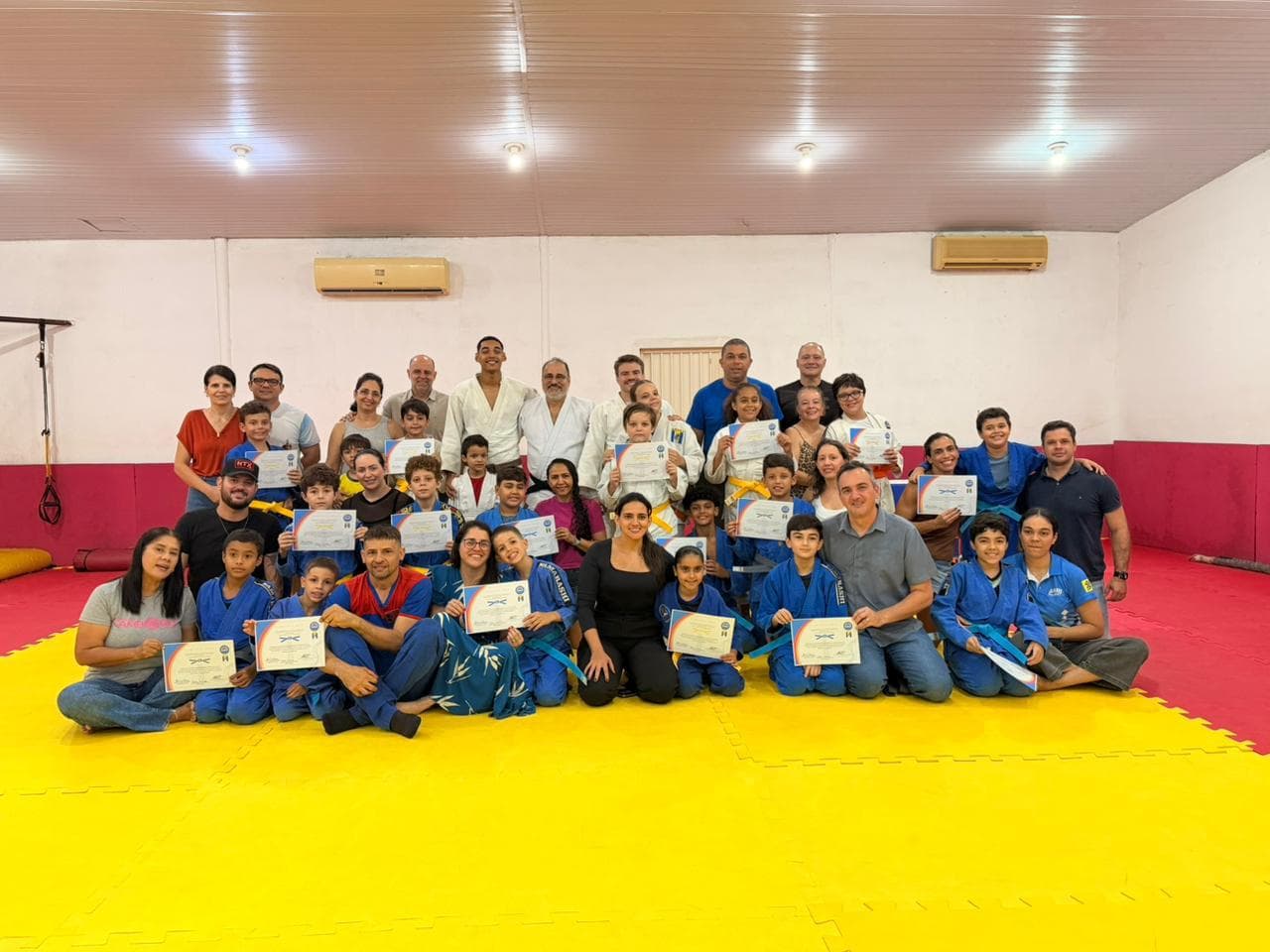Alunos, famílias e senseis reunidos no tatame com os certificados de formatura